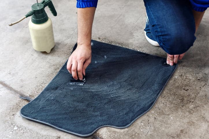 Details of automobile cleaning - male using professional chemical solutions to clean car floor mats.