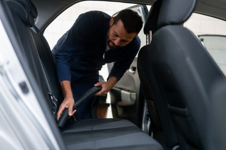 Man working at a car wash vacuuming the vehicle interior.