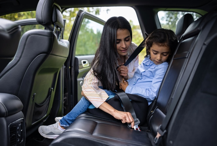 Loving mother buckling the seat belt of her daughter in the back seat of the car