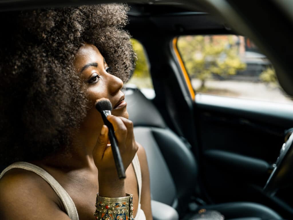 Young women in front seat of the car adjusting make up in car.