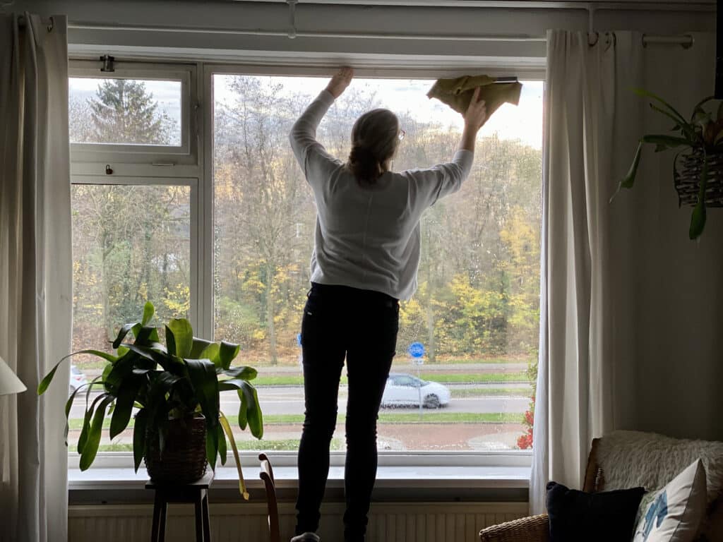 Women stood in on step ladders cleaning top of the living room window